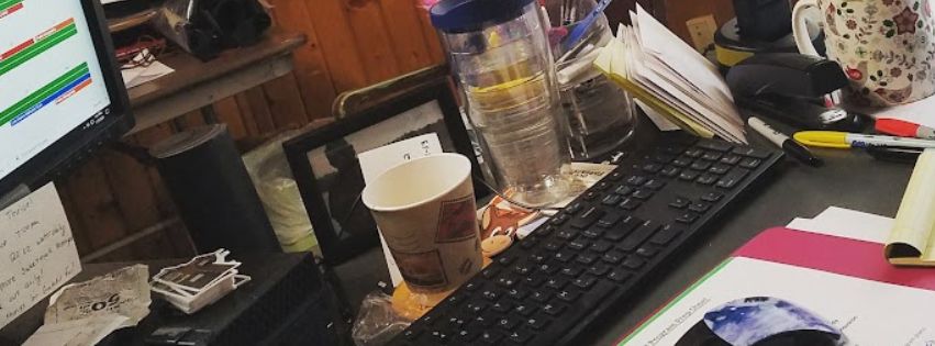 Kelby working at a cozy, cluttered desk with coffee and sticky notes